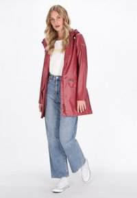 Punainen vedenpitävä sadetakki hupulla, etupainikkeet ja taskut, päällä valkoinen t-paita ja siniset korkeavyötäröiset farkut.