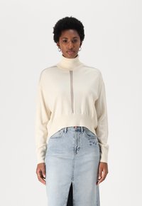 Krēmkrāsas augsta kakla džemperis ar ribotām piedurknēm un apakšmalu. Apvienots ar gaiši zilu denimā ražotu svārku, kam ir priekšējā iegriezuma un ziedu izšuvuma akcenti.