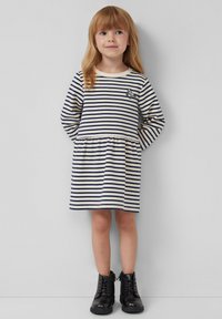 Gestreiftes langärmliges Kleid in Creme und Marine mit einem gerafften Bund, das eine kleine Tierstickerei aufweist. Schwarze Knöchelstiefel runden das Outfit ab.