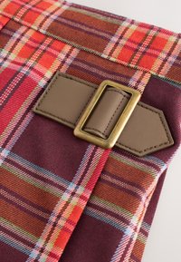 Tkanina w kratę w odcieniach czerwieni i brązów z zielonymi i niebieskimi akcentami, wyposażona w brązowy pasek ze sztucznej skóry i mosiężną prostokątną klamrę.