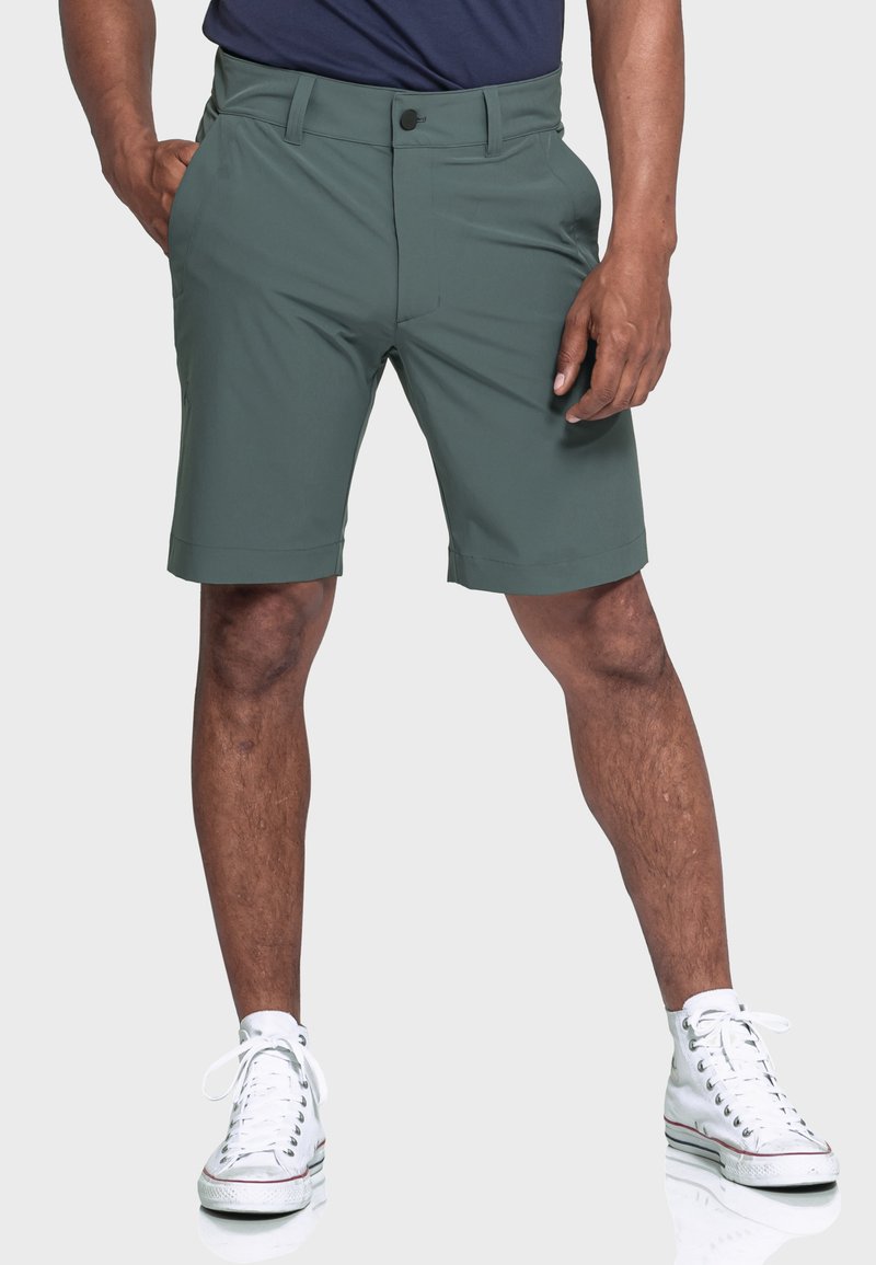 Grüne Shorts aus leichtem Material mit einem klassischen Design, einer Fronttasche und einem Knopfverschluss, kombiniert mit weißen High-Top-Sneakers.
