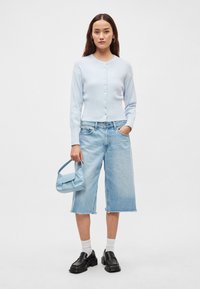 Απαλό γαλάζιο πλεκτό ζακέτα με στρογγυλή λαιμόκοψη και κλείσιμο με κουμπιά, συνδυασμένο με γαλάζια φαρδιά σορτς από τζιν και μια μικρή μπλε τσάντα. Μαύρα μοκασίνια και λευκές κάλτσες.