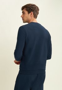 Sweatshirt côtelé bleu marine avec manches longues, col rond et coupe décontractée ; présente une texture douce et une finition soignée.