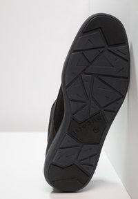 Suola nera in gomma con un motivo testurizzato, caratterizzata da disegni geometrici angolari e un logo. La parte superiore è realizzata in materiale a rete.