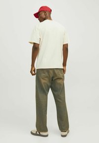 Beige bomulds t-shirt med korte ærmer, kombineret med løstsiddende grønne jeans og grå sneakers. En rød kasket bæres baglæns.