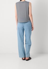 Top bez rękawów w granatowy geometryczny wzór, zestawiony z jasnoniebieskimi spodniami typu straight-leg. Czarne płaskie sandały; prosty design, casualowy wygląd.