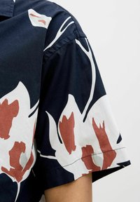 Camisa de manga corta de algodón en color navy con un patrón floral en blanco y óxido. Presenta un cuello doblado y un dobladillo cosido.