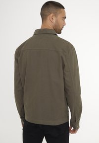 Olivenfarvet canvasjakke med krave, knapmanchetter og lige snit. Simpel design med synlige sømme og ingen mønstre.