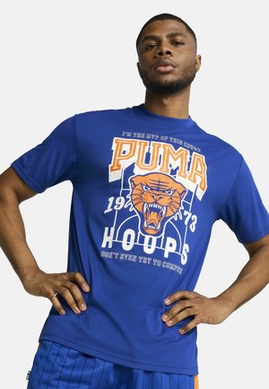 Blå kortærmet t-shirt med et grafisk motiv af en brølende tiger, "PUMA" tekst i orange og et basketball-tema. Blødt, strækbart materiale.