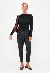 Zwarte langetees met lange mouwen, slim-fit ontwerp. Zwarte faux-leer broek met verstelbare tailleband. Bordeau-tas en schoenen maken de outfit compleet.