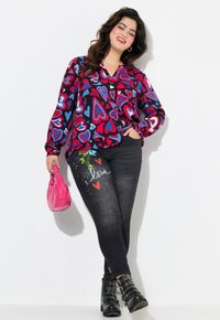 Blusa de manga larga colorida con estampados de corazones, combinada con jeans de mezclilla oscuros que presentan un diseño floral y la palabra "amor". Los accesorios incluyen un bolso rosa.