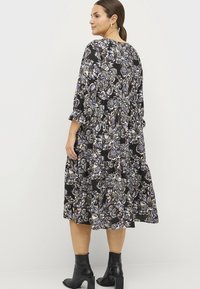 Zwart bloemen midi-jurk met lange mouwen, voorzien van een gelaagd ontwerp, paarse en witte patronen, en een ronde halslijn. Gepaard met zwarte enkellaarsjes.