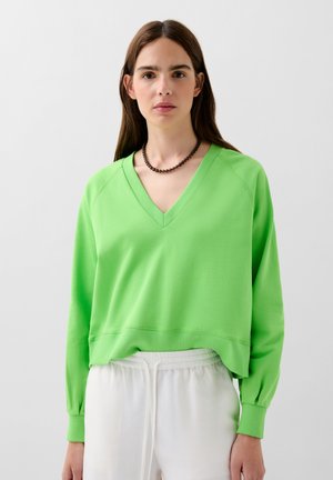 Groen V-hals sweatshirt met lange mouwen, geribbelde boorden en een cropped zoom. Soepele textuur, casual design, gecombineerd met lichtgekleurde broeken.