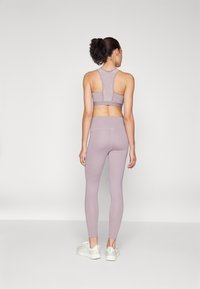 Lys lavendel treningssett inkludert en racerback sports-BH og høyt midje leggings, laget av et glatt, elastisk stoff. Hvite joggesko.