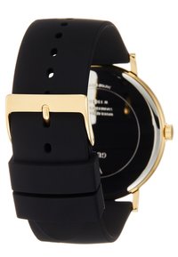 Bracelet de montre en silicone noir avec une quincaillerie et une boucle dorées. Boîtier rond avec un fond transparent affichant le mouvement. Texture mate.
