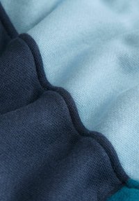 Tejido con un patrón ondulado en diferentes tonalidades de azul y marino, que muestra una textura suave y costuras entrelazadas.