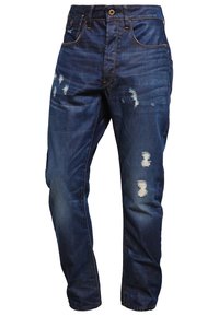 Jeans de mezclilla en un color azul oscuro, con textura desgastada y múltiples desgarros, cinco bolsillos y cierre de botón en la cintura.