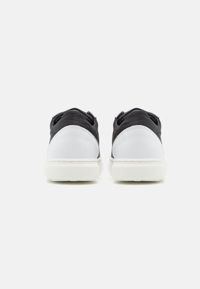 Zapatillas en blanco y negro con parte superior de cuero suave, puntera redondeada y suela de goma texturizada. Diseño minimalista con detalles de tela suave.