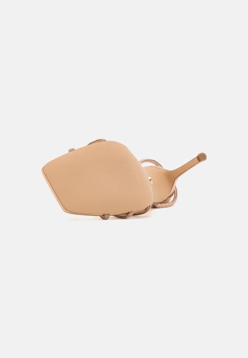 Sandalo beige con tacco alto, punta affusolata, suola testurizzata e sottili cinturini alla caviglia con dettagli metallici. Finitura liscia in tutto.