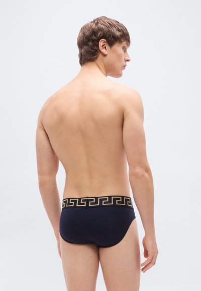 Μπλε ναυτικό μαγιό σλιπ με χρυστό γεωμετρικό σχέδιο στη μέση. Λείο ύφασμα, εφαρμοστή σχεδίαση και κλασική κοπή.