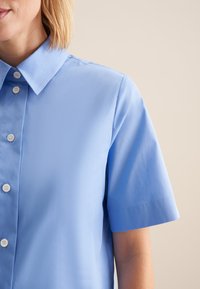 Jasnoniebieska koszula z krótkim rękawem z wyodrębnionym kołnierzykiem, o gładkiej fakturze i pięcioma białymi guzikami z przodu.