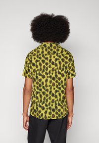 Camicetta a maniche corte di un verde brillante con motivo a macchie di leopardo nere. Dotata di colletto e vestibilità comoda. Tessuto liscio.