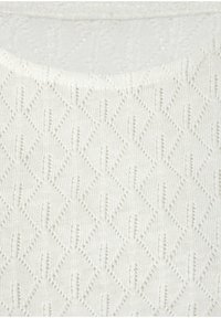 Weißer Strickstoff mit einem Rautenmuster, das eine erhabene Textur und kleine vertikale Schlitze aufweist, was ein kompliziertes Design schafft.