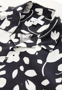 Zwart-witte bloempatronen shirt met een kraag, knoopdetails en een gladde textuur; heeft grote, abstracte bladeren en bloemen.