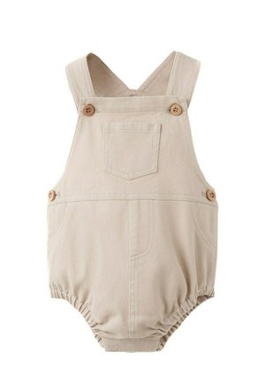 Combinaison courte beige en coton pour bébé avec bretelles, poche avant, boutons pression sur les côtés et les bretelles, et ouverture élastiquée aux jambes.