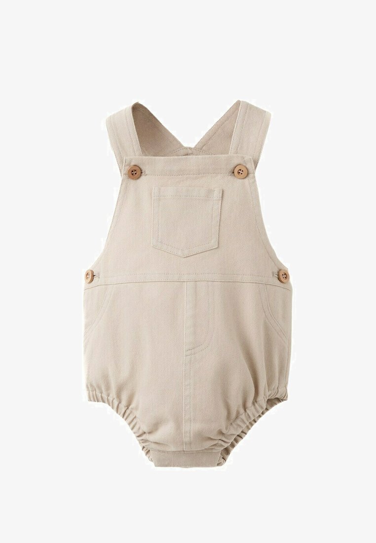 Béžový bavlnený detský overal s ramennými remienkami, predným vreckom, zapínaním na gombíky na stranách a na remienkoch, a s elastickými otvormi na nohy.