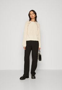 Strikket creme sweater med hulmønstre, rund halsudskæring og lange ærmer. Stylet med sorte cargo bukser og kraftige sorte sko.