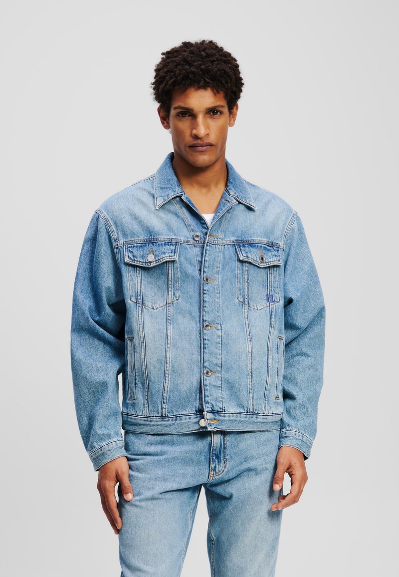 Ljusblå denimjacka med klassisk passform, som har två bröstfickor, knäppningar med knappar och en något urblekt yta.