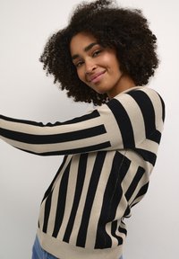 Pull rayé noir et beige à manches longues, fabriqué dans un matériau en tricot texturé ; présente un col rond et une coupe décontractée.