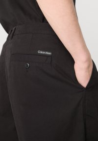Črne bombažne kratke hlače z zadnjim žepom s gumbom in majhno oznako Calvin Klein. Prilagojen kroj z gladko teksturo.