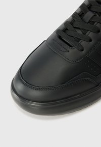 Zapatilla de cuero negro con un acabado suave, puntera redonda y acentos texturizados. Presenta cordones negros y detalles de costura minimalistas.