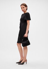 Melnas ceļu garuma kleitas ar īsām, izplešanās piedurknēm un sakrātu jostas detaļu, varēta ar mazu melnu kažokādas somiņu un smailām melnām kurpēm.