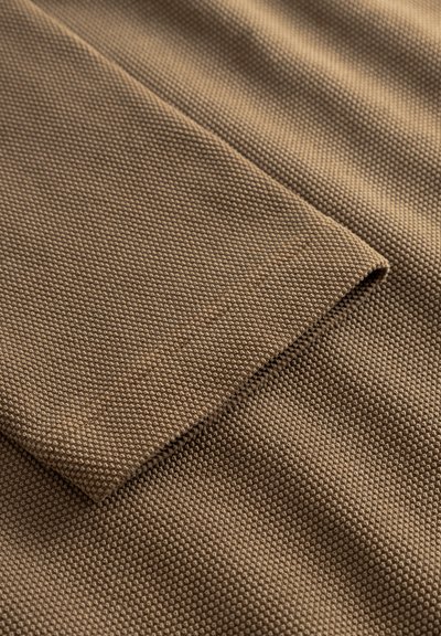 Barna texturált szövet szövött mintával és egy behajtott szegéllyel, bemutatva egy puha, tartós felületet. A szín gazdagságára és az anyag részleteire fókuszálva.