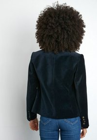 Námořnický sametový blazer se strukturovanými rameny, jediným švem na zadní straně a detaily tří knoflíků na manžetách. V kombinaci s modrými denimovými džíny.