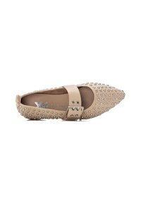 Zapato plano beige con punta afilada, adornado con tachuelas plateadas y una correa con hebilla en el empeine. Textura de cuero suave.