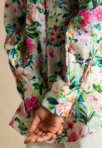 Camisa de botones con estampado floral en tela ligera, con un diseño botánico colorido en tonos rosa, verde y azul. Mangas largas, corte relajado.
