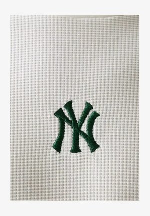 Logotipo "NY" entrelazado verde bordado sobre fondo de tela blanca texturizada.