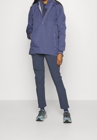 Lekka fioletowa kurtka z pół-zamkiem, kieszeniami bocznymi i dopasowanymi spodniami. Obuwie z szarymi i turkusowymi akcentami.