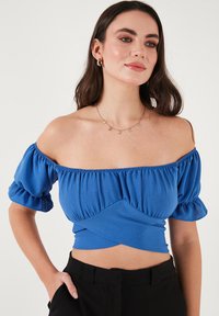 Blå off-the-shoulder top med puffærmer, samlet tekstur og en tætsiddende talje, lavet af et glat og let stof.
