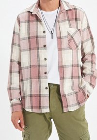 Geruit overhemd van zachte stof met roze, wit en zwart. Gevoerd met knopen aan de voorkant, lange mouwen en een enkele borstzak.