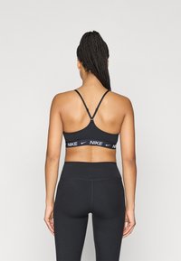 Nike sporta krūšturis melnā krāsā ar baltu logo, ar regulējamām lencēm un sacīkšu aizmugures dizainu. Gluda tekstūra ar piegulošu siluetu.