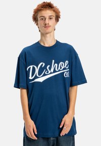Navyblå oversized t-shirt i bomull med vit "DCshoe Co." logotyp tryckt över framsidan. Korta ärmar och rund halsringning.
