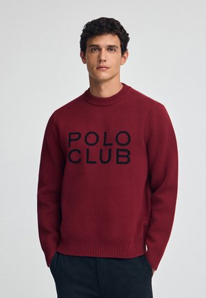 Maglione rosso a collo rotondo realizzato in tessuto lavorato a maglia, con un logo nero "POLO CLUB" al centro. Polsini e orlo a coste.