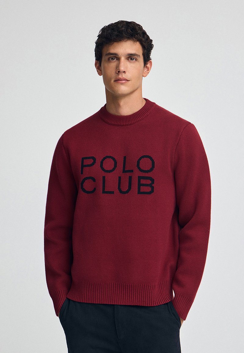 Roter Rundhals-Pullover aus strukturiertem Strickstoff, mit einem schwarzen "POLO CLUB"-Logo in der Mitte. Rippbündchen an den Ärmeln und am Saum.