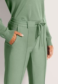 Lichtgroene joggers met een tailleband met trekkoord, zijzakken en een gestructureerde stof. Kenmerken zijn taps toelopende benen en contrasterende stikseldetails.