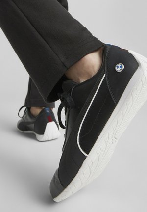 Baskets en cuir noir avec semelle blanche, présentant un accent bleu et rouge au talon et une texture perforée sur le dessus.